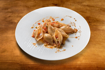 Italian pasta conchiglioni cooked with tomato sauce and vegetables in white plate on wooden table