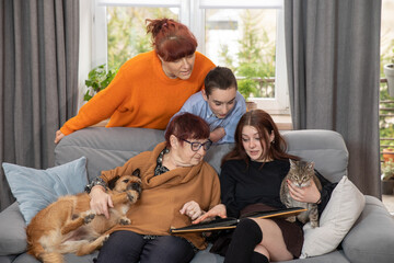 Family is looking at photo book in the living room. Grandma and her grandchildren looking at photo...