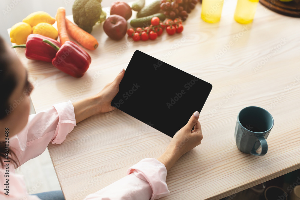 Poster Woman using tablet with empty screen for mockup in kitchen