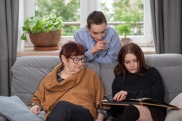 Family is looking at photo book in the living room. Grandma and her grandchildren looking at photo album together at home.