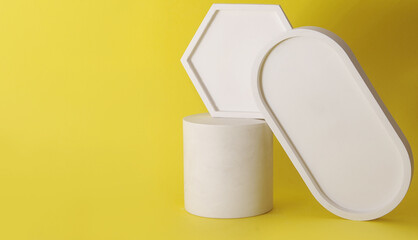 Podium of white cylinder with geometric shapes on yellow background.