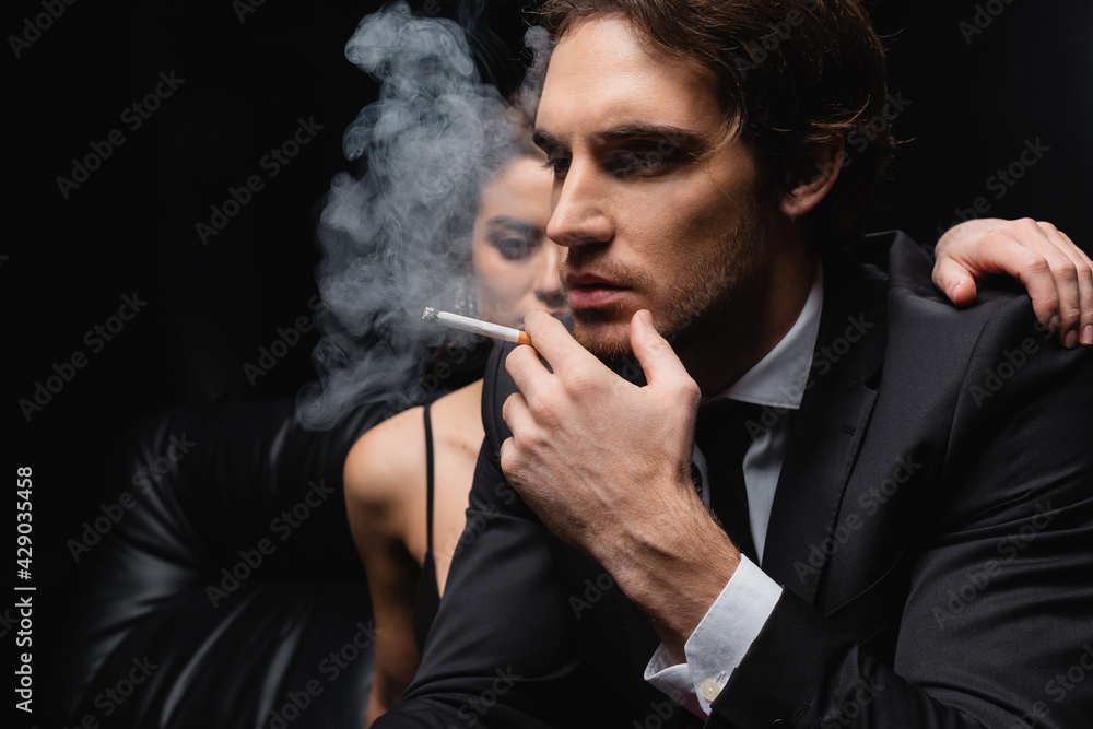 Wall mural man in suit smoking cigarette near woman on blurred black background.