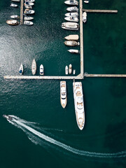 Fototapeta na wymiar Aerial top down view of boat dock and yacht port in Budva, Montenegro. White private motor boats are moored to pier on Adriatic sea coast. Yacht club boats parking. Photo from drone. Minimalism.