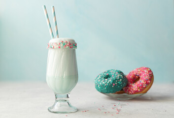 blue milkshake in a glass cup and striped straws. Next to it is a doughnut with a bright sprinkle.