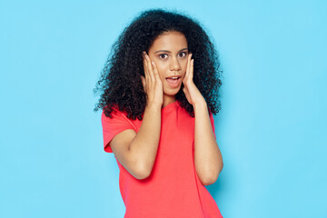 frightened woman with open mouth and in a red t-shirt touches her face with her hands on a blue background
