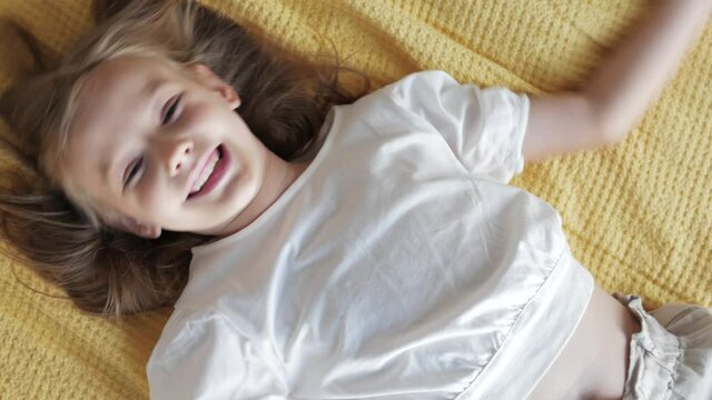 Portrait of a cute little girl lying on bed and looking at camera, smiling, laughing. Positive emotions of the girl baby. The smile of a happy child. Concept of happy childhood, carefree children 
