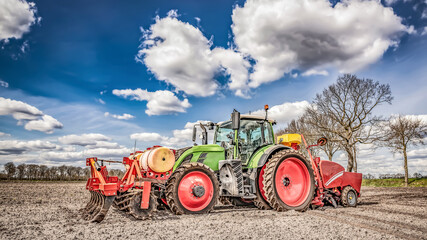 Obraz premium Large, green, modern tractor from Germany sowing potatoes in the field on a sunny spring day