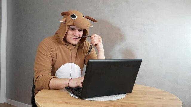 Office worker in cosplay costume of a cow. Guy in the funny animal pyjamas sleepwear near the laptop. Man is working from home. Search job, unemployment  concept, economy crisis. Remote work.