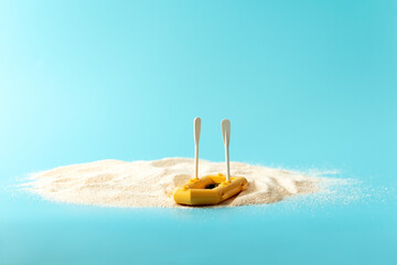 Tropical beach concept made of sand and boat with paddles on blue background. Creative summer vacation concept