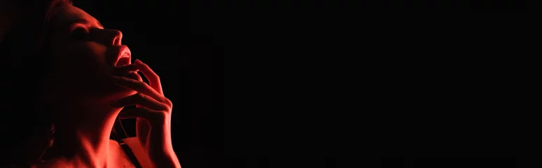 rote beleuchtung auf verführerischer frau, die lippen berührt, isoliert auf schwarz, banner. © LIGHTFIELD STUDIOS