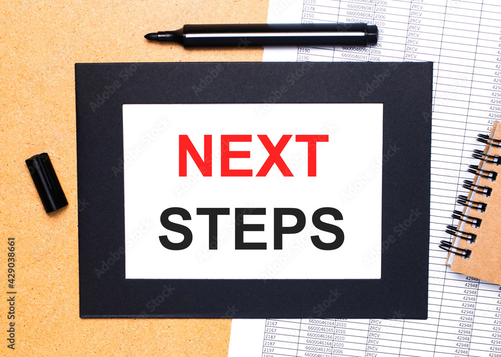 Poster on a wooden table, there is a black open marker, a brown notepad and a sheet of paper in a black fra
