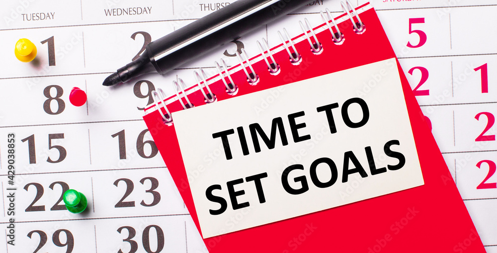 Aufkleber on the calendar is a white card with the text time to set goals. nearby is a red notepad and a marke