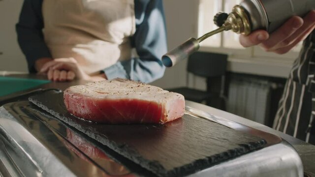 Slowmo closeup of chef cooking seared tuna steak using manual gas burner, showing master class at culinary school