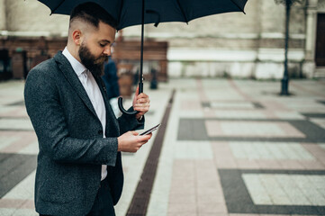 Businessman using a smartphone and holding a black umbrella
