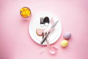 Easter holiday table setting on a pink background, top view. Plates with colorful eggs. Easter holiday concept.