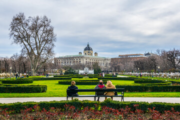 People are sitting on a bench in the famous Volksgarten (People's Garden) public park with museum...