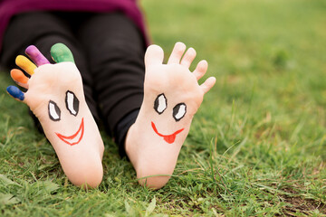 Child have fun outdoor on grass. Feet of child with painted smile faces.