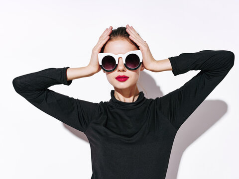 woman model in a black sweater and sunglasses holds her hands on her head