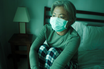 home dramatic portrait of  attractive middle aged woman 50s with grey hair and protective mask during covid-19 virus lockdown quarantine sitting on couch  thoughtful