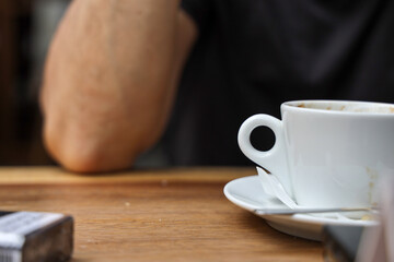 Closeup of coffee on wooden table, selective focus; man is drinking coffee.
