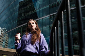 Young woman in a purple hooded sweat drinking a coffee in the street.