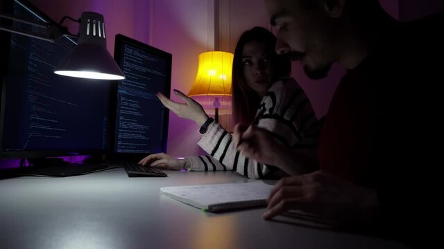 Cooperation of two IT workers who are coding new program on computer. Team job of man and woman developing software. A woman is typing on the keyboard and man is talking to her. Concept of cyberspace