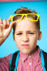 schoolboy in yellow glasses with a backpack and a pink shirt on a blue background