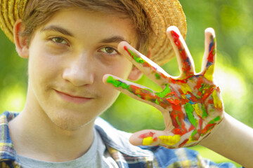 a young European guy shows a palm painted with multi-colored oil paints against the background of a...