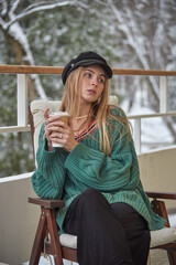 A girl with blonde hair sits at a table with a cardboard cup.