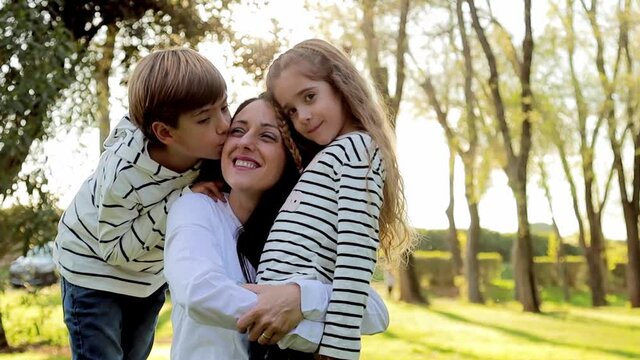 Adorable kids hug their mom in the park