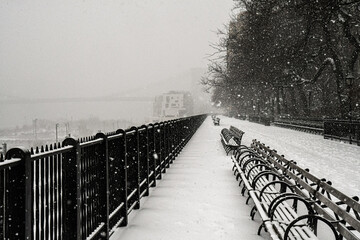Snowfall on the benches of the Brooklyn Promenade with the Brooklyn Bridge silhouetted in the...