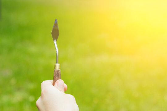 the hand of a European artist holds a mastekhin smeared in oil paint against the background of a green lawn. Blurred background. copy space - Powered by Adobe