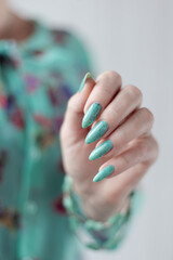 Female hand with long nails and light blue turquoise manicure with bottles of nail polish