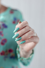 Female hand with long nails and light blue turquoise manicure with bottles of nail polish