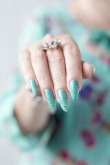Female hand with long nails and light blue turquoise manicure with bottles of nail polish