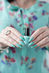 Female hand with long nails and light blue turquoise manicure with bottles of nail polish