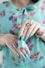 Female hand with long nails and light blue turquoise manicure with bottles of nail polish