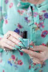 Female hand with long nails and light blue turquoise manicure with bottles of nail polish