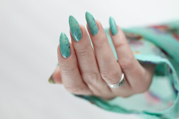Female hand with long nails and light blue turquoise manicure with bottles of nail polish
