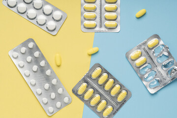Yellow and white pills on blue and yellow background, top view. Different medicines, tablets, medicine capsules. Medicine concept, background. Flat lay