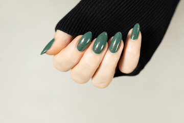 Female hand with long nails and green manicure with bottles of nail polish