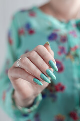 Female hand with long nails and light blue turquoise manicure with bottles of nail polish