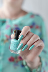 Female hand with long nails and light blue turquoise manicure with bottles of nail polish