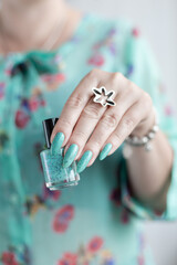 Female hand with long nails and light blue turquoise manicure with bottles of nail polish