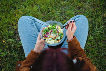 Teenager girl eating a salad while sitting on grass. She is enjoying the calm. Shot from above.