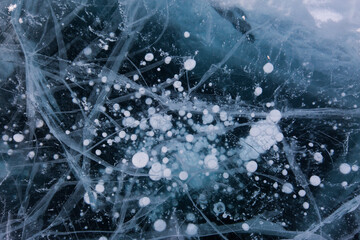 Frozen Baikal lake with cracks and methane bubbles on the transparent ice surface. Winter abstract and blue ice background.