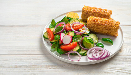 Fresh salad with vegetables and corn on a flat white plate on a light background with space to copy.