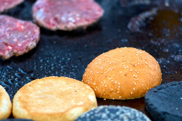 black, yellow buns and raw hamburger patties in a frying pan, close-up, street food