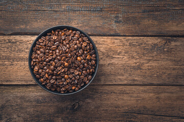 Coffee beans in a bag and ground coffee in a cup on a wooden table with space to copy.