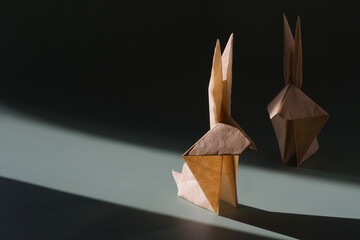 Origami paper rabbit in the bright sun with hard shadows. Crafts made of paper. The minimal concept of Easter or the year of the rabbit. The play of light and shadow